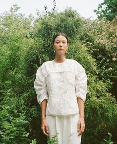 a woman standing in front of some bushes