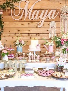 a table topped with cakes and desserts covered in frosted icing next to a wooden wall