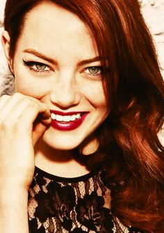 a woman with red hair and green eyes smiles at the camera while wearing a black lace top