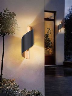 an outdoor wall light that is on the side of a building with trees in front of it