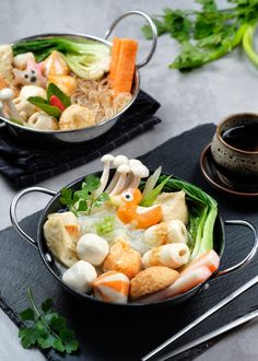 two pans filled with different types of food on top of a black cloth next to chopsticks