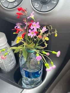 a vase filled with colorful flowers sitting on top of a car dash board next to an air freshener dispenser