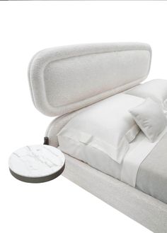 a bed with white sheets and pillows on top of it next to a round table