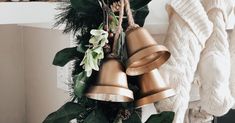 a bunch of bells are hanging from a mantle with greenery and pine cones on it