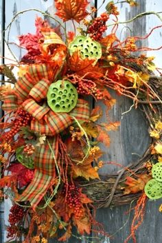 a wreath that is hanging on the side of a wooden door with leaves and other decorations