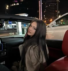 a woman sitting in the driver's seat of a car at night with her hand on the steering wheel