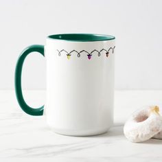 a white and green coffee mug sitting next to a donut