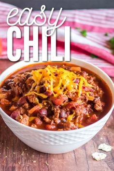 a white bowl filled with chili and cheese on top of a wooden table next to an orange