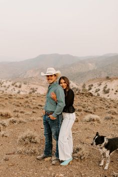 a man and woman are standing in the desert with a dog looking at the camera