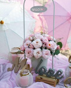 a welcome sign and pink flowers in a pot on a table with umbrellas behind it