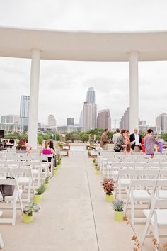 an outdoor ceremony with white chairs and green planters in front of the city skyline