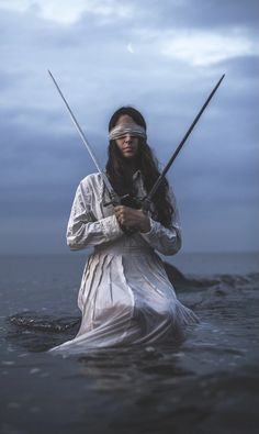 a woman with two swords standing in the water