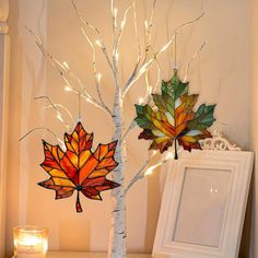 two stained glass maple leaf ornaments hanging from a tree next to a lit up candle