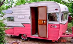 an old pink and white trailer parked in the woods with its door open to reveal another room