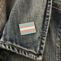 a blue, pink and white striped pin sitting on top of a pair of jeans