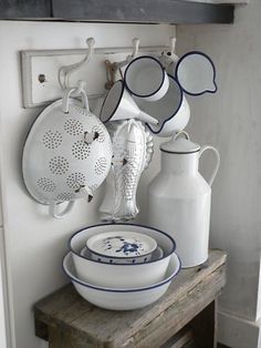 white and blue dishes are sitting on a wooden shelf in front of a wall mounted pot rack