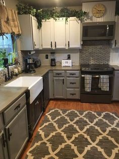 a kitchen with white cabinets and gray counters, an area rug in front of the sink