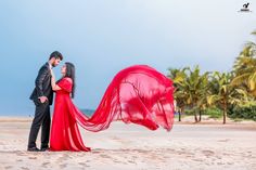 a man and woman standing on top of a beach next to each other holding a red scarf