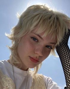 a woman with short blonde hair wearing a white shirt and black netted arm warmer