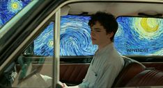 a young man sitting in the passenger seat of a car with a painting on the wall behind him