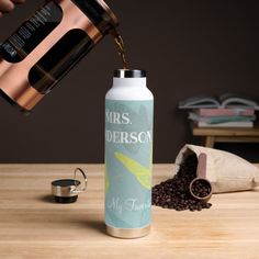 a person pouring coffee into a white water bottle on top of a wooden table next to a bag