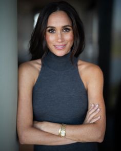 a woman with her arms crossed wearing a black top and gold bracelets, looking at the camera