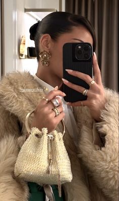 a woman taking a selfie with her cell phone while wearing a fur coat and holding a purse