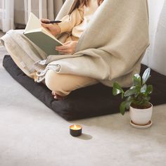 a woman is sitting on the floor reading a book and holding a candle in her hand