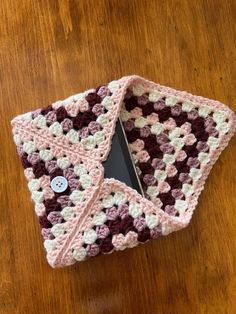 two crocheted squares are sitting on top of a wooden table with a button in the middle