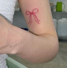 a woman's arm with a red bow tattoo on the left side of her arm