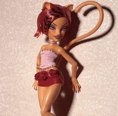 a doll with red hair wearing a pink top and skirt, holding a cat tail