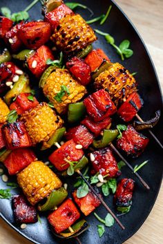 a black plate topped with skewers of food on top of a wooden table