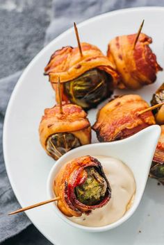 an appetizer plate with bacon wrapped vegetables and dip in a small white bowl