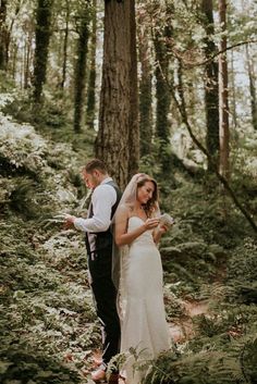 a bride and groom standing in the woods