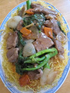 a blue and white plate topped with meat, veggies and noodles covered in sauce