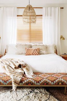 a bed with white sheets and pillows in a bedroom next to a window covered by curtains