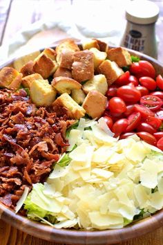 a wooden bowl filled with lots of different types of salads and toppings next to a bottle of ketchup