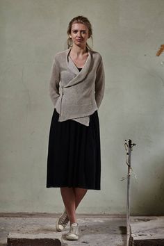 a woman standing in front of a wall wearing a sweater and skirt with an asymmetrical design