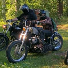 two motorcyclists wearing helmets are parked in the grass next to each other