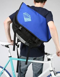 a man carrying a blue bag on his back while standing next to a bicycle in front of him