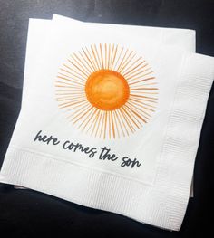 there is a napkin with the words here comes the sun on it and an orange sun