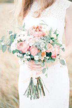 a woman holding a bouquet of flowers in her hands and wearing a white wedding dress