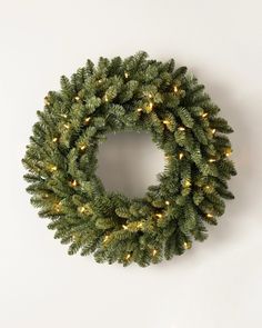 a christmas wreath with lights hanging from it's sides on a white wall background