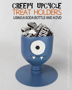 a blue cup filled with candy sitting on top of a white table next to the words creepy upcycle treat holders using soda bottle and dvd