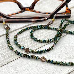 "Shiny and bohemian eyeglass necklace chain in green and copper tones with multicolor flashes, made with Preciosa Czech crystal seed beads and copper plated flower Hematite gemstone charms.      Paired with beautiful delicate copper plated Japanese Miyuki crystal seed beads, this handmade eyeglass chain will definitely create a unique look. This eyeglass lanyard is made on strong quality beading wire with gold plated wire guardians that protect the quality white eyeglass holder grips. The neckla Bohemian Gold Glasses Chains With Colorful Beads, Green Glass Festival Jewelry, Handmade Green Glass Bead Glasses Chains, Handmade Green Glasses Chains With Round Beads, Bohemian Glasses Chains With Colorful Round Beads, Green Round Beaded Glasses Chains For Gifts, Adjustable Green Bohemian Glasses Chains, Green Glasses Chains With Round Beads For Gift, Handmade Green Glass Glasses Chains