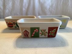 three ceramic dishes with christmas designs on them sitting on a white tablecloth covered surface