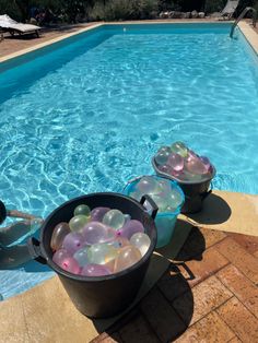 two buckets filled with balloons sitting next to a swimming pool