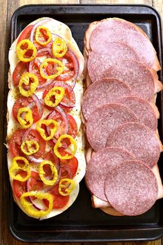 two hot dogs and some sliced sausages on a black tray with wood table top