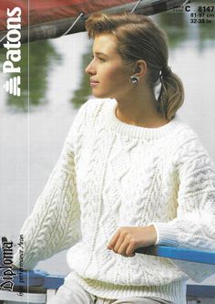 a woman sitting on top of a boat next to a body of water wearing a white sweater