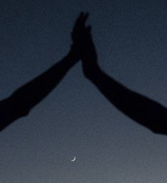 two people reaching their hands up to the sky at night with a half moon in the distance